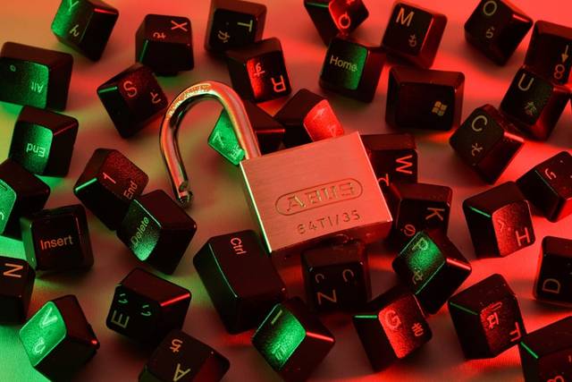 Un candado metálico abierto entre teclas sueltas de un teclado, todo iluminado con luz roja y verde